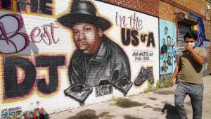 A person wearing a surgical mask walks past a mural of Jam Master Jay in New York.