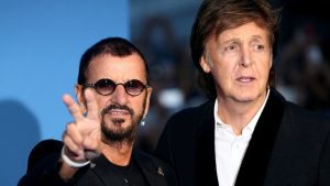 Ringo Starr (left) holds his hands in a peace sign, standing next to Paul McCartney at a movie premiere